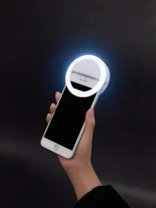 Hand holding a smartphone with a glowing clip-on selfie ring light against a dark background, highlighting portable mobile photography accessories and trending products India for content creators and selfie lovers.
